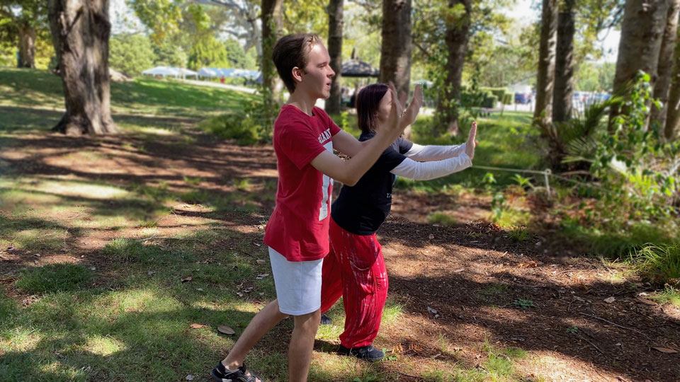 Teenage boy in red shirt doing tai chi in the park surrounded by trees